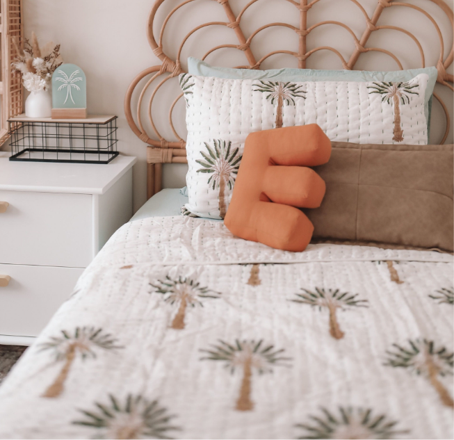 Bed with palm tree patterned bedding and pillows, featuring a decorative 'E' pillow.