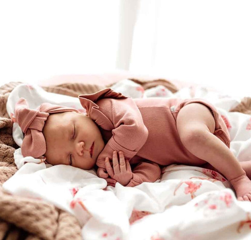 Newborn baby in pink outfit with large bows sleeping on a floral blanket